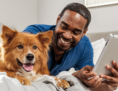 Man and dog laying on bed looking at Ipad
