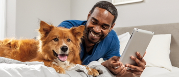 Man and dog laying on bed looking at Ipad